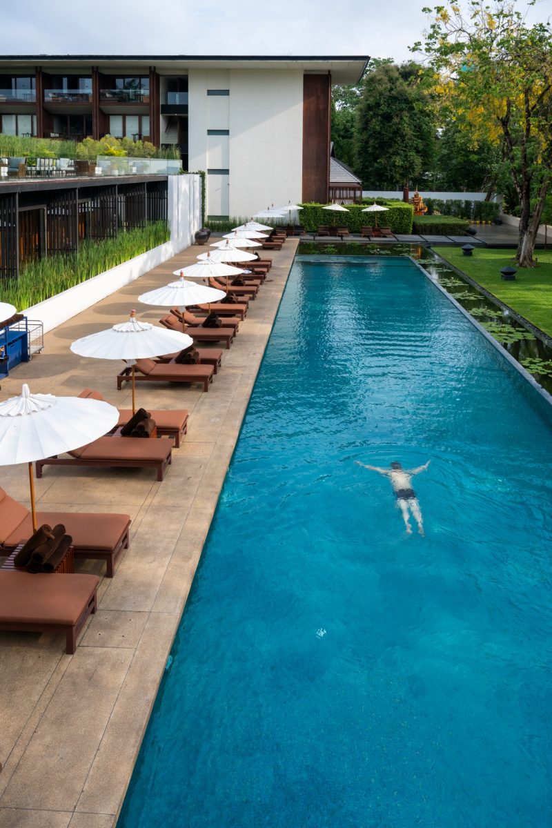 สระว่ายน้ำพร้อมร่มสีขาวและเตียงอาบแดด