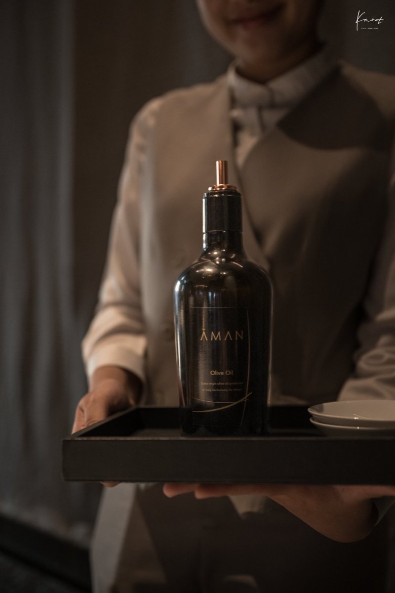 พนักงานเสิร์ฟถือขวด Aman Olive Oil ซิกเนเจอร์ของห้องอาหาร Aman