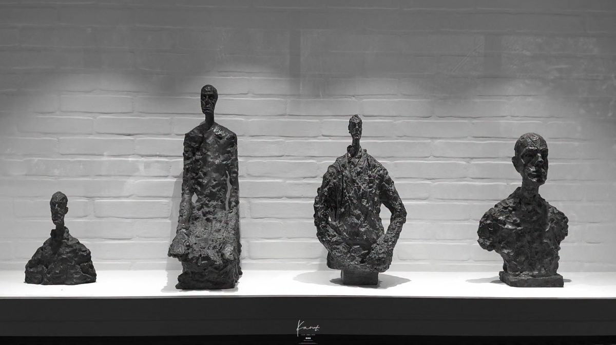 ประติมากรรมของ Alberto Giacometti หลายชิ้นเรียงบนชั้นยาวในห้องผนังขาว