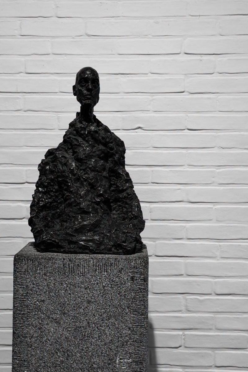 รูปปั้นครึ่งตัวของ Alberto Giacometti บนแท่นหิน หน้าผนังอิฐสีขาว